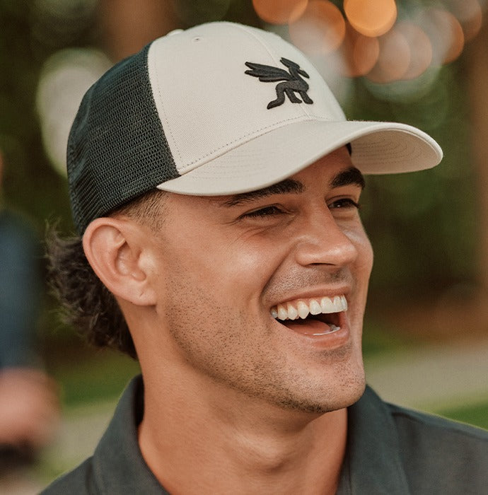 Man laughing in a cream and forest Signature dragon trucker cap