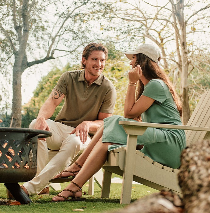 A couple in Signature apparel laughing beside a backyard fire pit